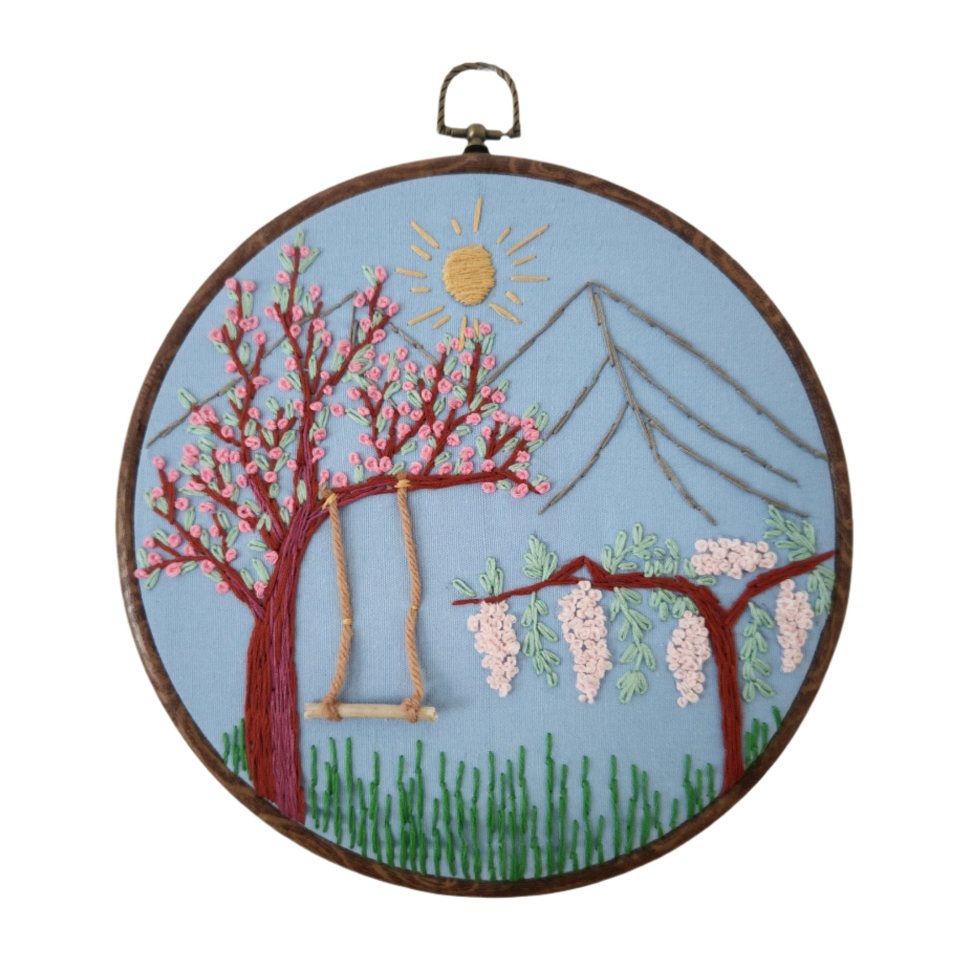 Embroidered hoop art with cherry blossom tree and wisteria against a blue sky.
